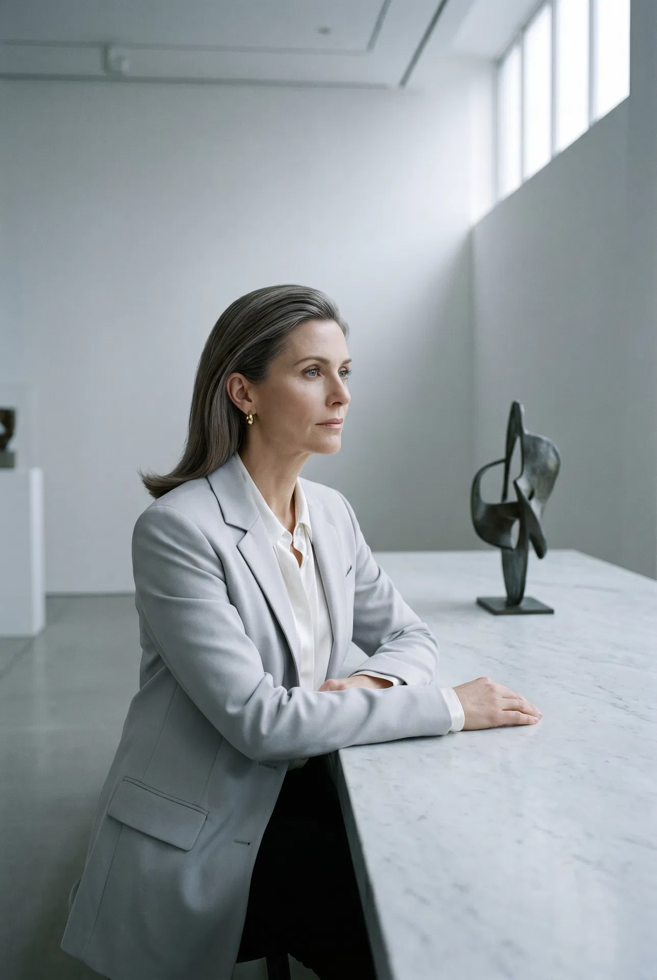 Lin — Hair Topper model, cool-neutral brown hair at marble table in gallery